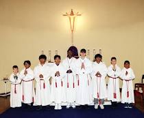 Group of clergy in white robes posing in a church with a crucifix behind them.